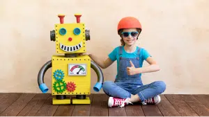 An image of a child sitting on the floor beside a yellow cardboard smart toy robot.
