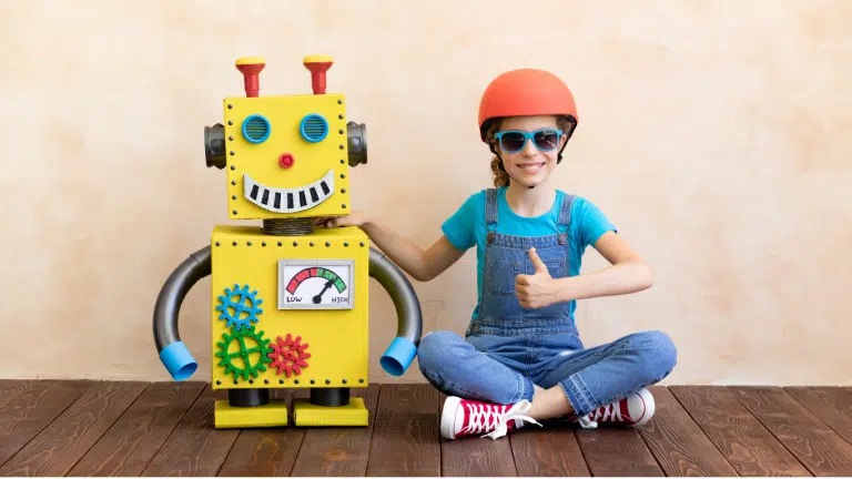 An image of a child sitting on the floor beside a yellow cardboard smart toy robot.