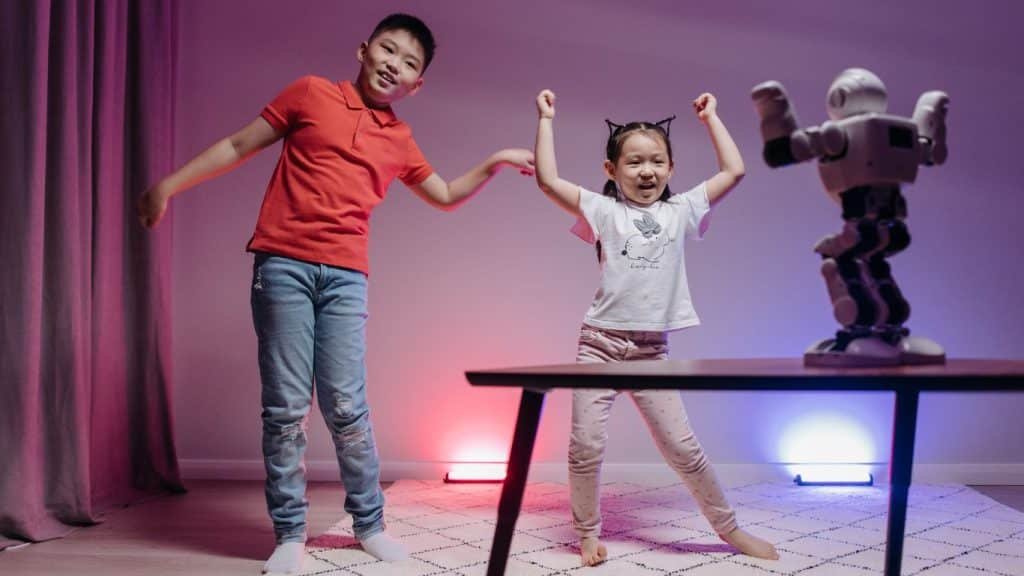 Two joyful children, a boy and a girl, excitedly interacting with an interactive robot on a table in a room, showcasing a playful scene that enhances emotional intelligence through technology.